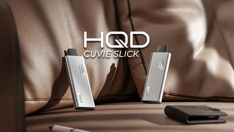 2 HQD Cuvie Slick disposable vapes on a brown leather sofa with a wallet and pen around it
